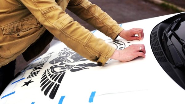 Клеит виниловую наклейку на авто